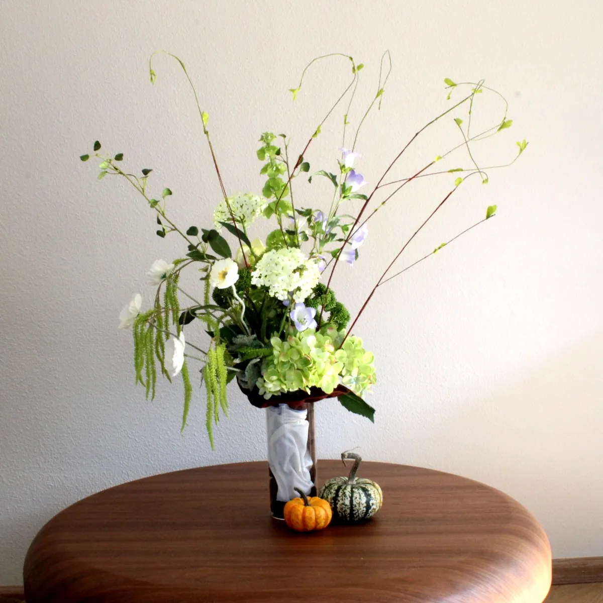 Boeket van zijdebloemen in groen, wit en lila in een glazen vaas
